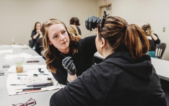 A cosmetology student is practicing makeup application on another student